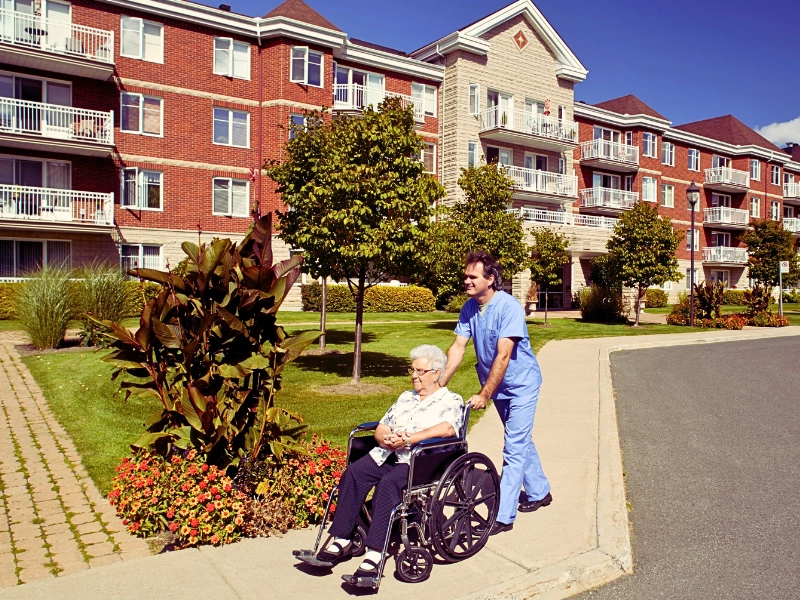 nurse pushing woman in wheel chair outside a nursing home