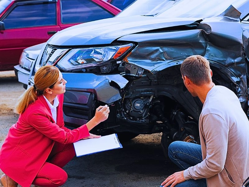 Man reporting and insurance agent filling claim form near broken car outdoors.