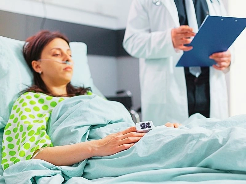 Hospitalized woman with finger heart rate monitor showing pulse while resting in bed.