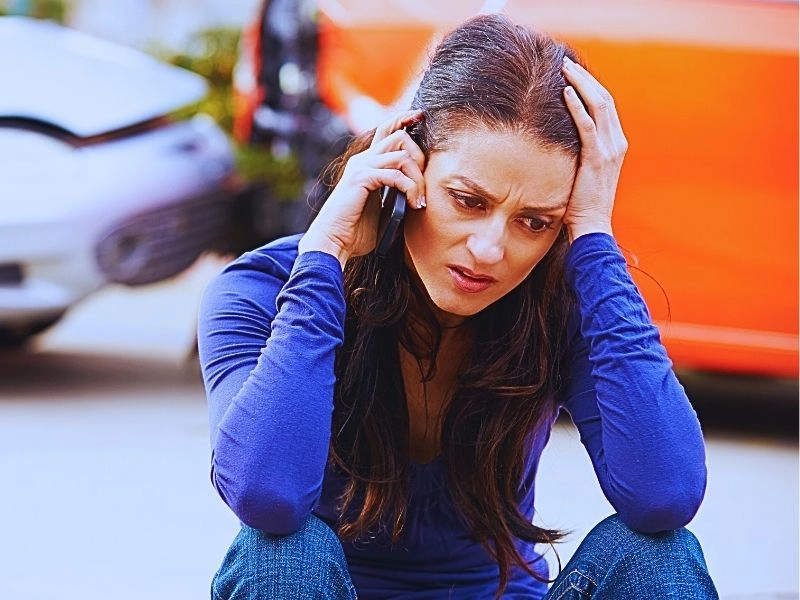 Female driver making phone call after traffic accident with head in hands.
