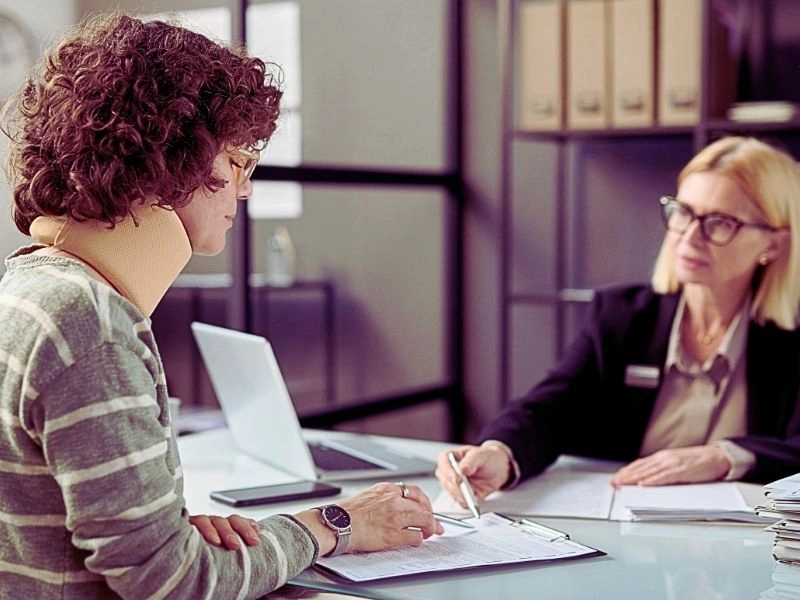Young woman with neck injury filling documents with her lawyer.