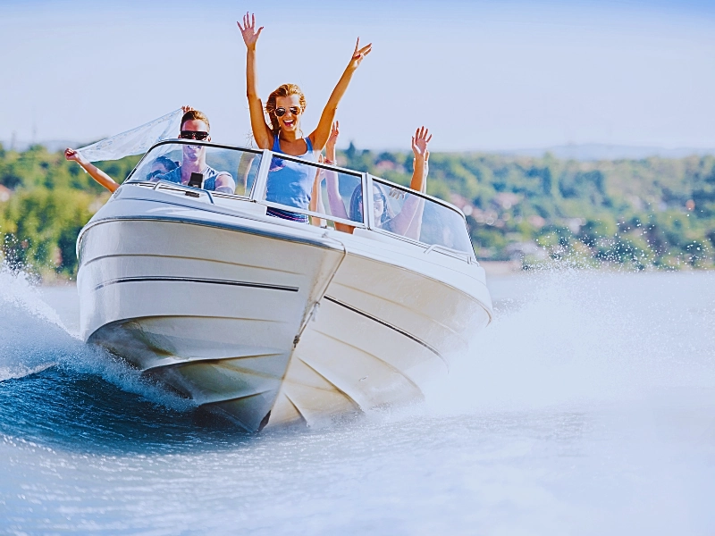 Group of young people with raised hands enjoying in a speedboat ride.