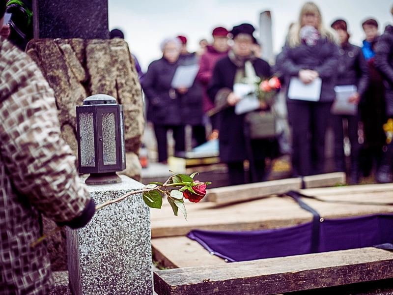 Mourners at a funeral holding flowers near a gravesite