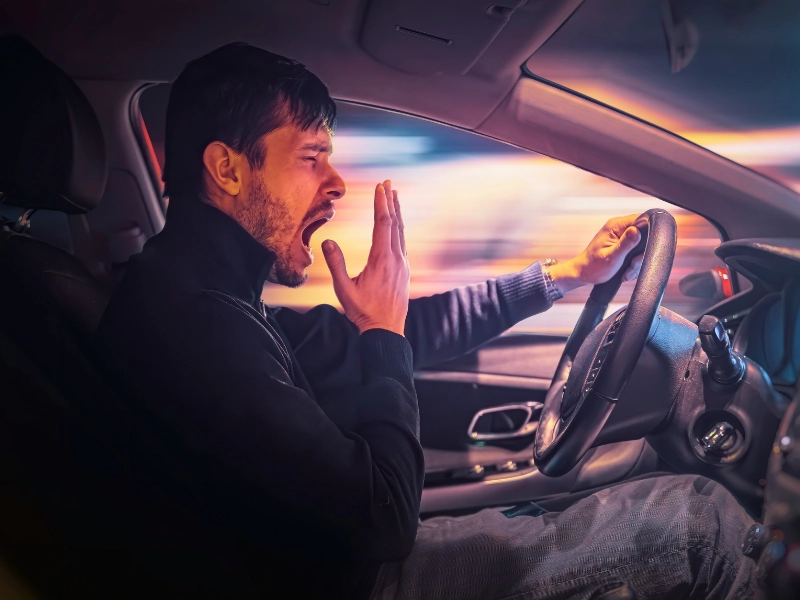 Young sleepy man is yawning and driving car at night. drowsy driving
