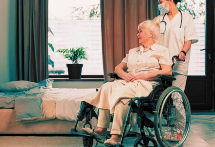 Nurse assisting an elder woman on a wheelchair in her bedroom. Sue for a Loved One's Bedsores