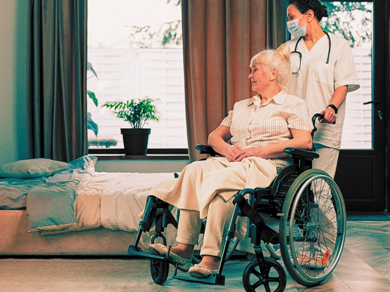 Nurse assisting an elder woman on a wheelchair in her bedroom. Sue for a Loved One's Bedsores