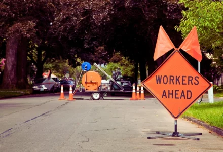 Orange and Black "Workers Ahead" Sign in Residential Neighbourhood with Equipment in the background. road construction zones