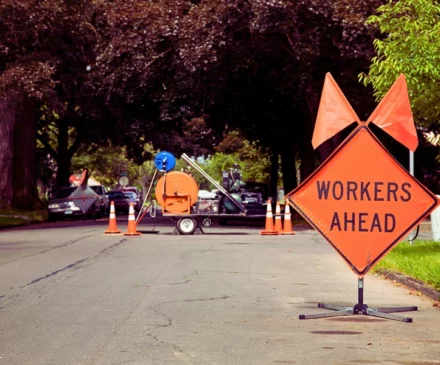 Orange and Black "Workers Ahead" Sign in Residential Neighbourhood with Equipment in the background. road construction zones