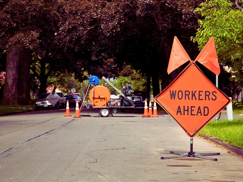 Orange and Black "Workers Ahead" Sign in Residential Neighbourhood with Equipment in the background. road construction zones