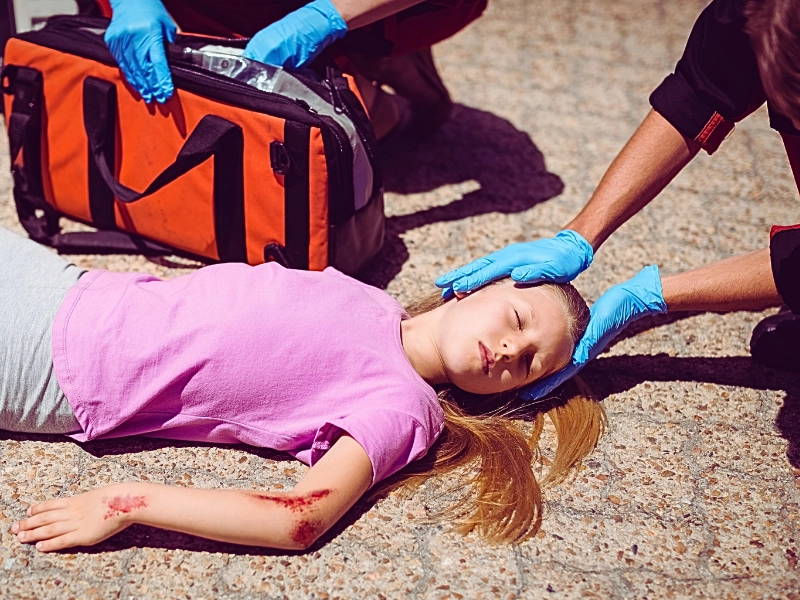 Paramedics examining injured girl on street. Your Child Is Injured in a Car Accident