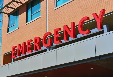 The word "EMERGENCY" in large, bold red letters mounted on the exterior of a building, likely indicating the entrance to an emergency department of a hospital or medical facility.