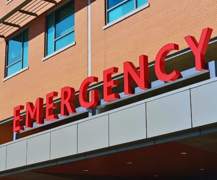 The word "EMERGENCY" in large, bold red letters mounted on the exterior of a building, likely indicating the entrance to an emergency department of a hospital or medical facility.