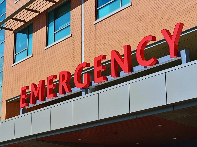 The word "EMERGENCY" in large, bold red letters mounted on the exterior of a building, likely indicating the entrance to an emergency department of a hospital or medical facility.