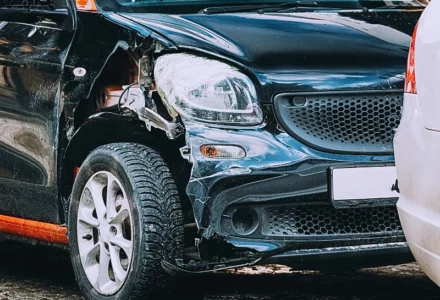 a black vintage car with visible damage on its front left side. The front left fender is dented, and the headlight area appears broken. Third-Party Claims