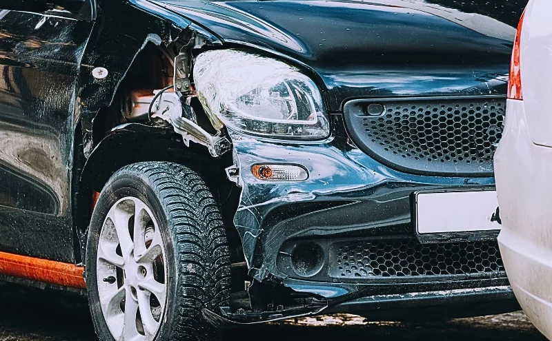 How Third-Party Claims Work After a Workplace Vehicle Accident 1 a black vintage car with visible damage on its front left side. The front left fender is dented, and the headlight area appears broken. Third-Party Claims