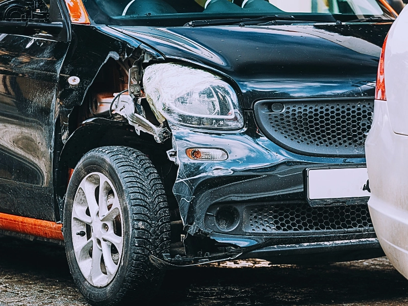 a black vintage car with visible damage on its front left side. The front left fender is dented, and the headlight area appears broken. Third-Party Claims