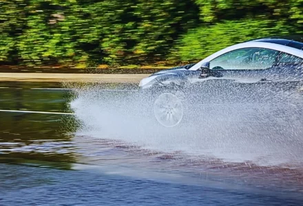 a silver car hydroplaning on a wet road, with water splashing dramatically from the tires. Wet Roads Lead to Naperville Collisions