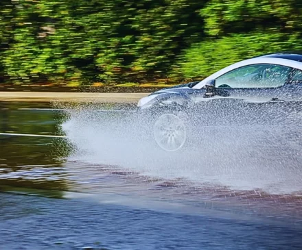 a silver car hydroplaning on a wet road, with water splashing dramatically from the tires. Wet Roads Lead to Naperville Collisions
