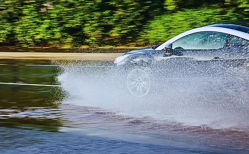 Hydroplaning and Flooded Streets: Why Wet Roads Lead to Naperville Collisions 1 a silver car hydroplaning on a wet road, with water splashing dramatically from the tires. Wet Roads Lead to Naperville Collisions