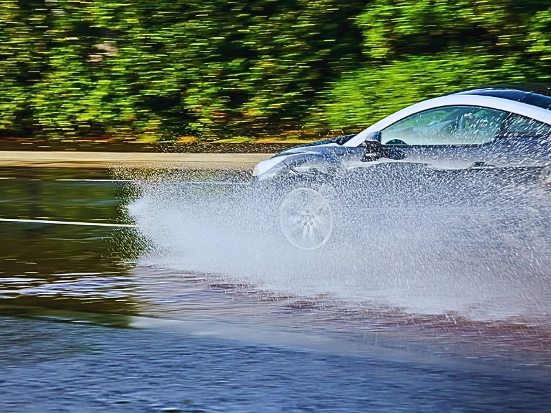 a silver car hydroplaning on a wet road, with water splashing dramatically from the tires. Wet Roads Lead to Naperville Collisions