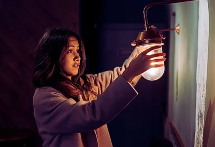 a young woman standing indoors, reaching out with both hands to hold a small wall lamp. Poor Lighting Accident