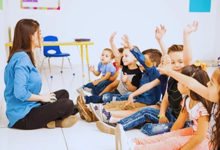 a group of young children sitting on the floor in a classroom setting, all raising their hands as if eager to participate or answer a question. Daycare Injuries