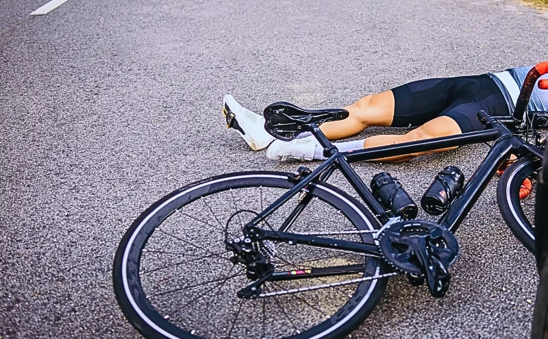 cyclist lying on the road next to a fallen bicycle, indicating a serious hit-and-run accident.
