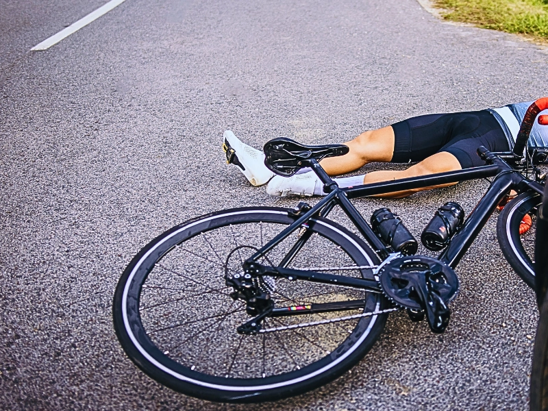 cyclist lying on the road next to a fallen bicycle, indicating a serious hit-and-run accident.