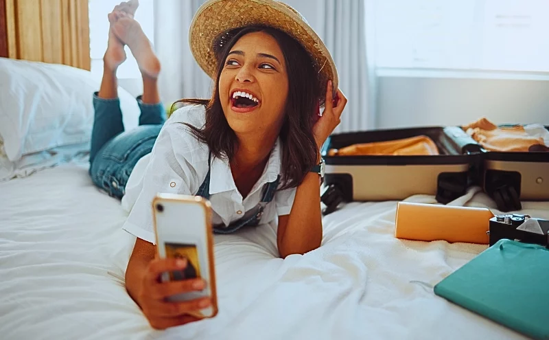 a woman lying on a bed in a hotel room, holding a smartphone in her hand. Airbnb Injury Lawyer