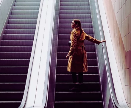 a woman standing alone on an escalator going up inside a building. Injured on an Elevator