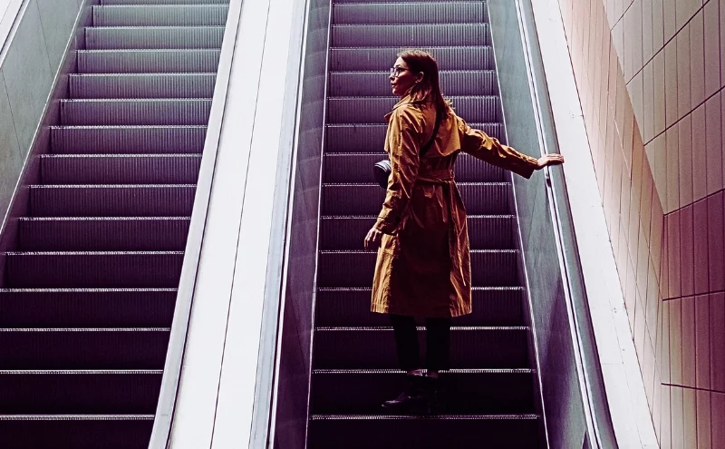 a woman standing alone on an escalator going up inside a building. Injured on an Elevator