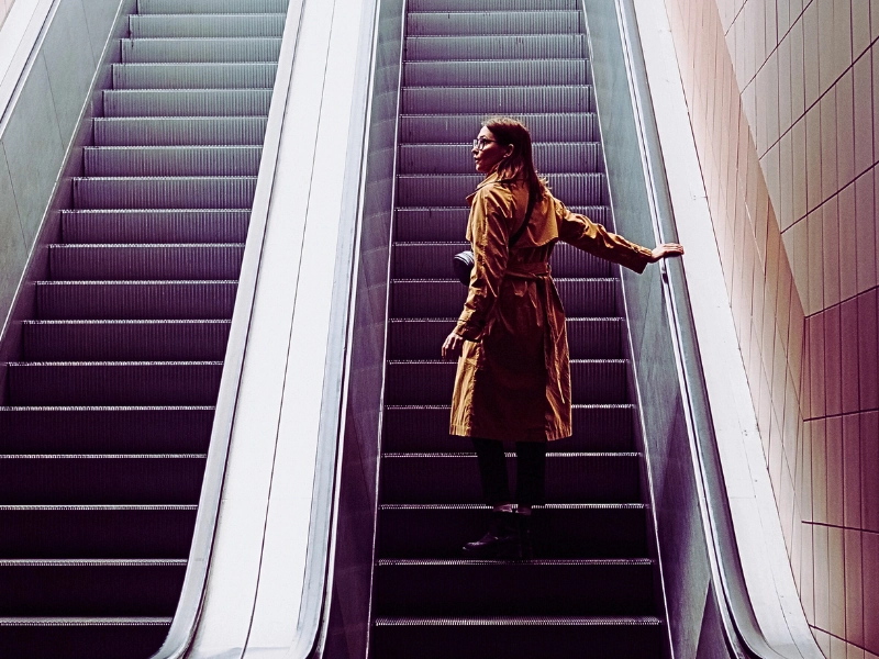 a woman standing alone on an escalator going up inside a building. Injured on an Elevator