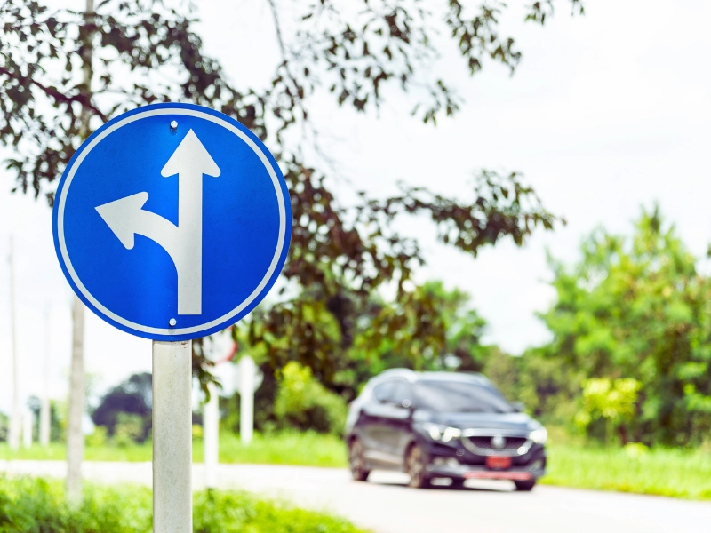 A blue circular traffic sign with two white arrows: one pointing straight ahead and the other curving left. Left-Turn Accidents