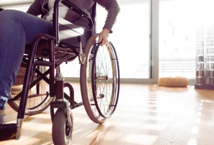 A person using a wheelchair indoors on a wooden floor, with natural light coming through large windows. Permanent Disability After an Injury