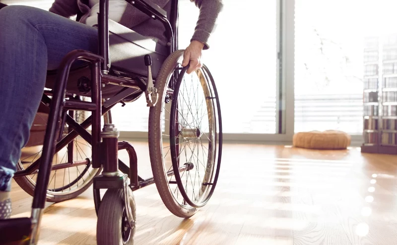 A person using a wheelchair indoors on a wooden floor, with natural light coming through large windows. Permanent Disability After an Injury