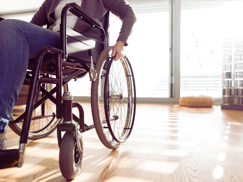 A person using a wheelchair indoors on a wooden floor, with natural light coming through large windows. Permanent Disability After an Injury