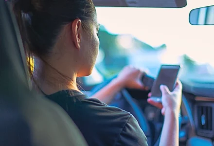 A person sitting in the driver's seat of a car, holding and looking at a smartphone. If the Other Driver Was Texting
