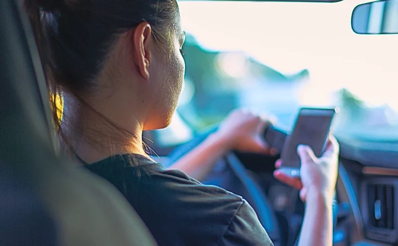 A person sitting in the driver's seat of a car, holding and looking at a smartphone. If the Other Driver Was Texting