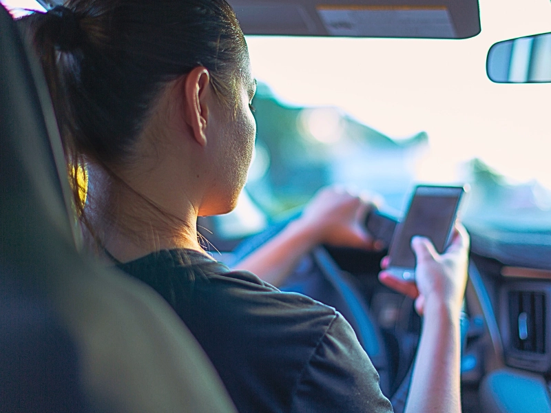 A person sitting in the driver's seat of a car, holding and looking at a smartphone. If the Other Driver Was Texting