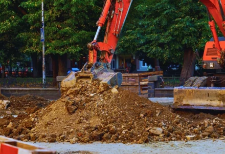 An orange excavator bucket moving a pile of dirt.