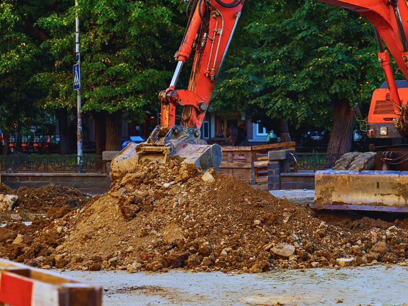 An orange excavator bucket moving a pile of dirt.
