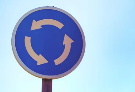 Blue circular traffic sign with white arrows showing roundabout. Crash in a Naperville Roundabout