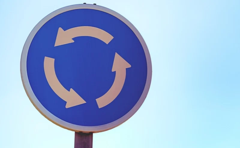 Who Is Liable for a Crash in a Naperville Roundabout? 1 Blue circular traffic sign with white arrows showing roundabout. Crash in a Naperville Roundabout