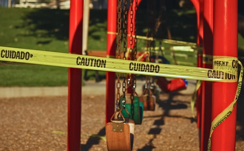 Yellow caution tape wrapped around a closed playground swing. Unsafe Playground Equipment