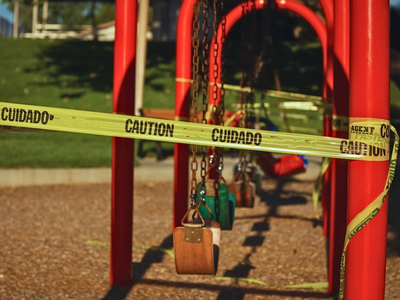 Yellow caution tape wrapped around a closed playground swing. Unsafe Playground Equipment
