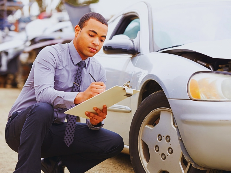 Insurance adjuster inspecting and writing on clipboard near damaged car. insurance company denies your car accident claim