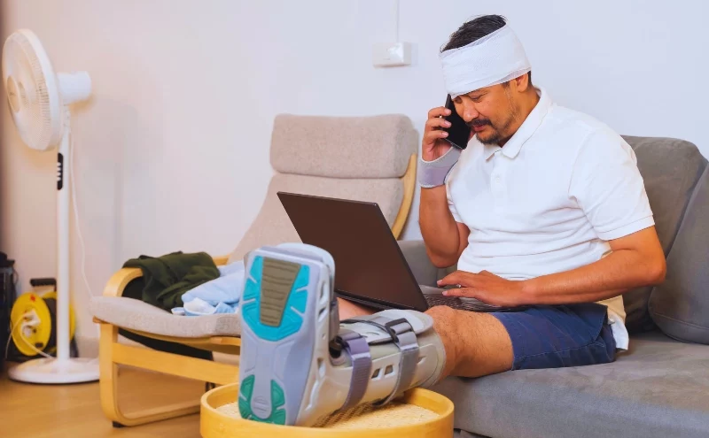What If the Insurance Company Downplays Your Injuries After a Car Accident in Illinois? 1 Injured man with bandages and boot working from home. insurance company downplays your injuries after a car accident insurance company downplays your injuries after a car accident, downplays car accident injuries, minimizes your injuries