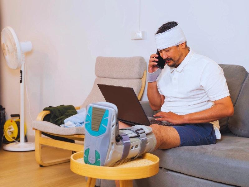 Injured man with bandages and boot working from home. insurance company downplays your injuries after a car accident insurance company downplays your injuries after a car accident, downplays car accident injuries, minimizes your injuries