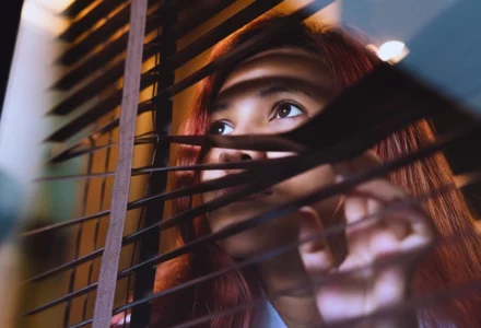 Woman peering curiously through the slats of window blinds. workers' compensation investigators follow you