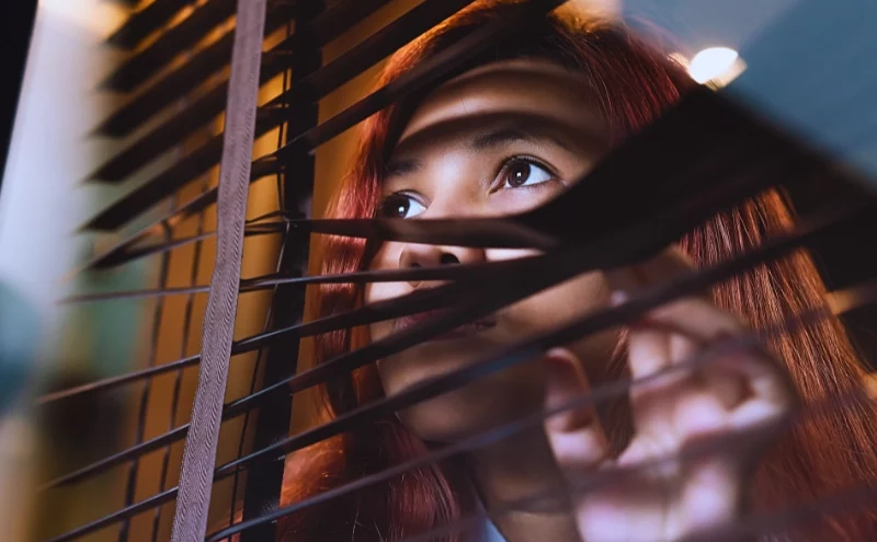 Can Workers Compensation Investigators Follow You in Illinois? 1 Woman peering curiously through the slats of window blinds. workers' compensation investigators follow you
